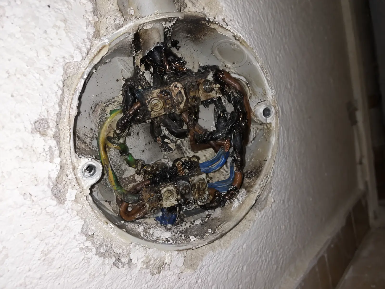 Caja de registro abierta en la pared con las regletas de empalme ennegrecidas y el aislamiento de los cables derretido