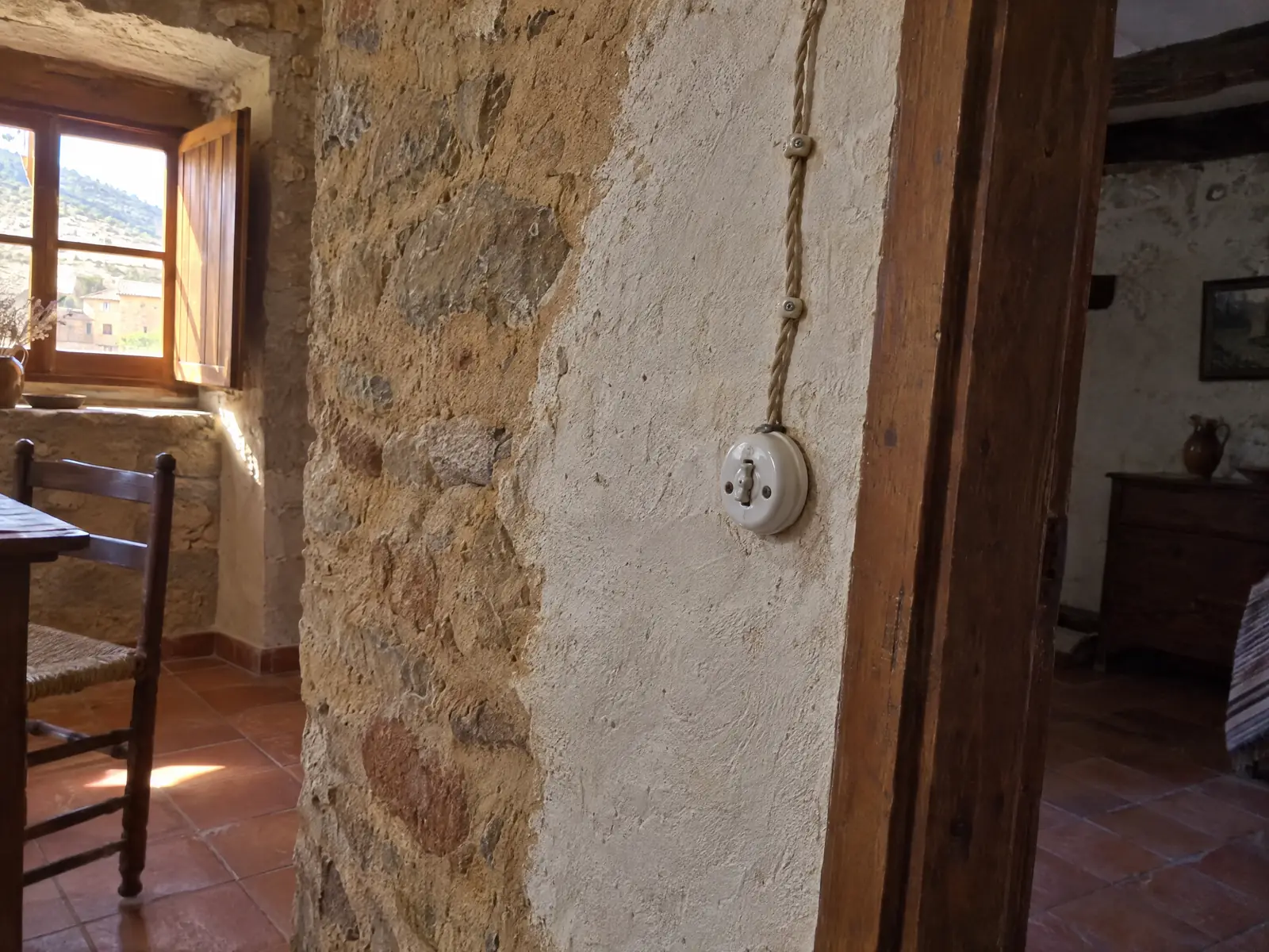 Casa de pueblo con muro de piedra, interruptor de porcelana antiguo y cable trenzado en superficie, suelo de barro cocido